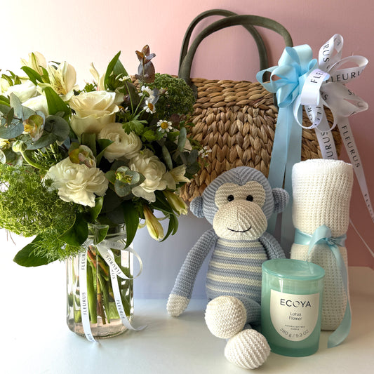 Baby boy gift basket contents with white flowers, blue monkey plush, white blanket and Ecoya candle