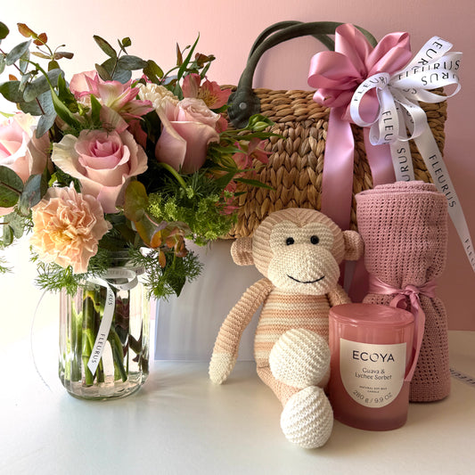 Baby girl gift basket contents with pink flowers, pink Loui monkey, rose cotton blanket and Ecoya Guava & Lychee candle