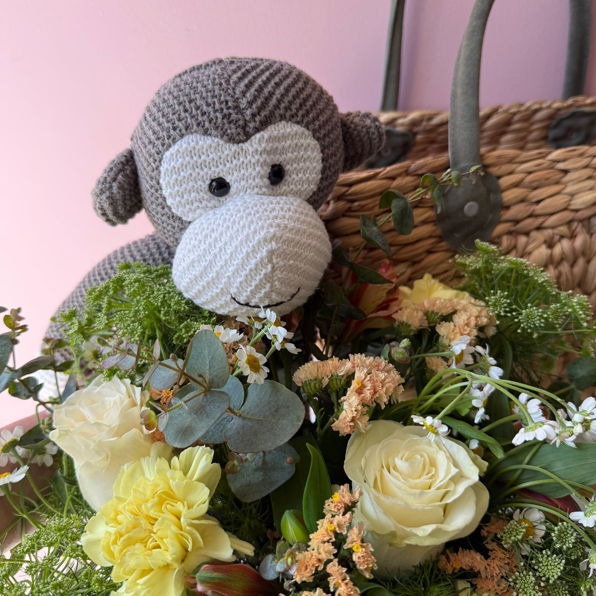 Close-up of brown Loui the Monkey plush toy with cream roses, yellow flowers and foliage