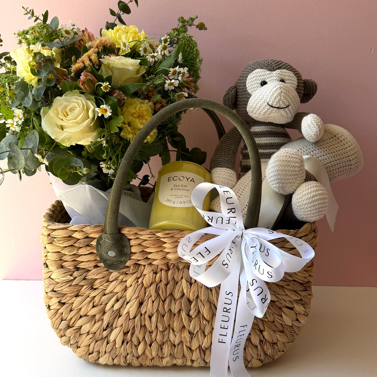 Neutral baby gift basket with fresh flowers, brown monkey plush, natural blanket and Ecoya candle arranged in a woven market basket