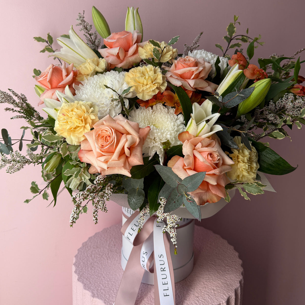 Apricot and peach seasonal flowers arranged in a white Fleurus hat box.