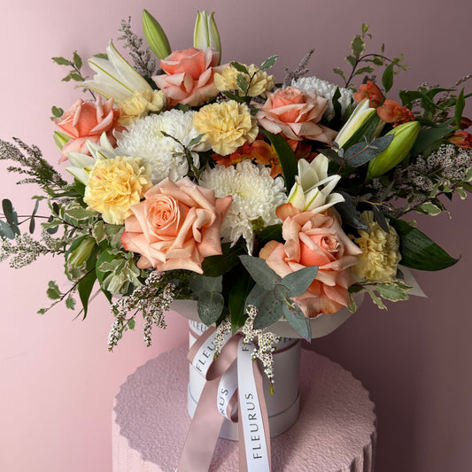 Apricot and peach seasonal flowers arranged in a white Fleurus hat box.
